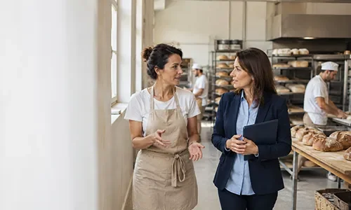 Asesora y propietaria de una panadería artesanal recorriendo las instalaciones del negocio mientras analizan sus necesidades de financiación